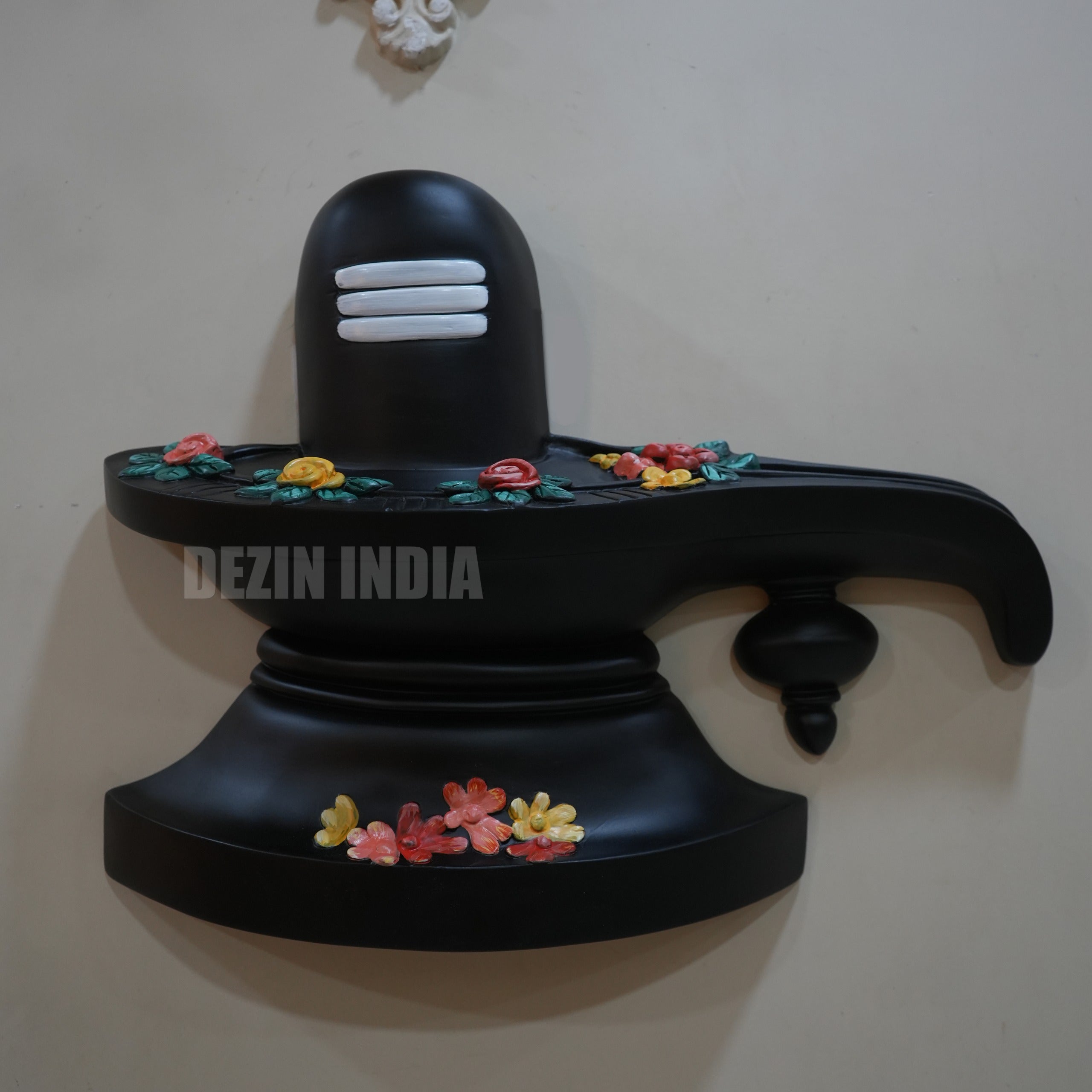 Black Shiva Lingam with colorful flowers on a white wall, branded 'Dezin India'.
