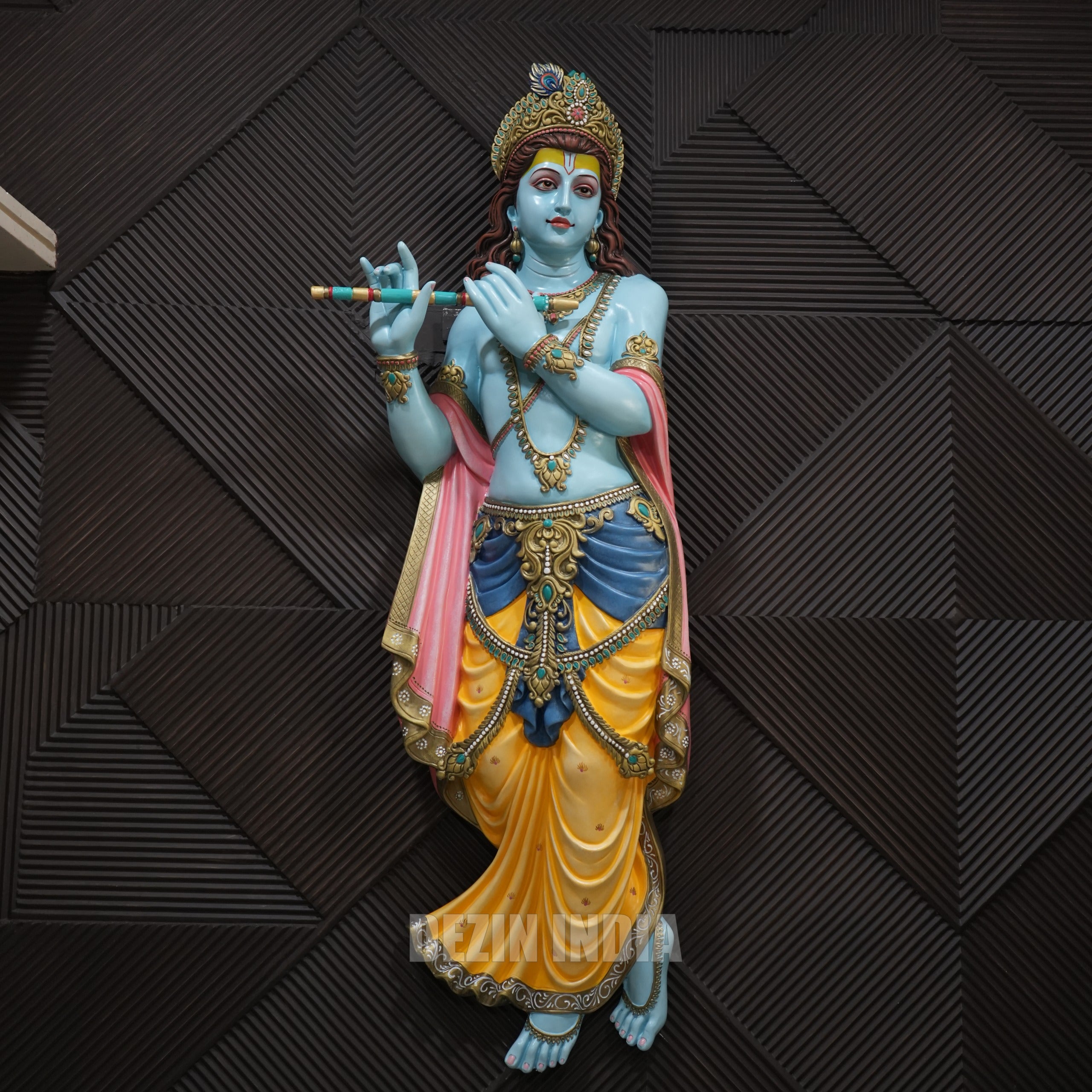 Colorful statue of a deity holding a flute against a dark geometric-patterned background